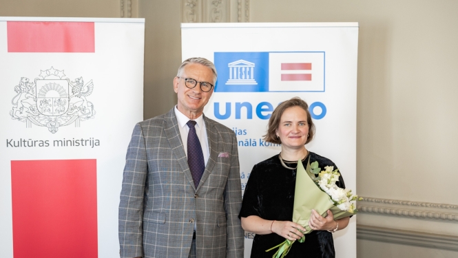 Nauris Puntulis un Dace Resele ar baltu ziedu pušķi, fonā Kultūras ministrijas un UNESCO Latvijas Nacionālās komisijas baneri.