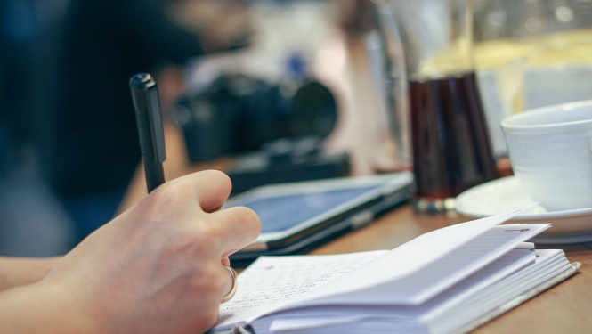 Klade, kurā cilvēka roka raksta ar pildspalvu.