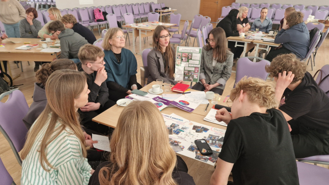 Semināra dalībnieki sēž pie galda apļveida formā un diskutē.