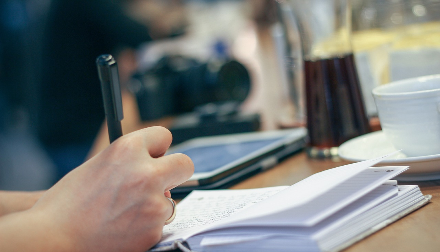 Klade, kurā cilvēka roka raksta ar pildspalvu.