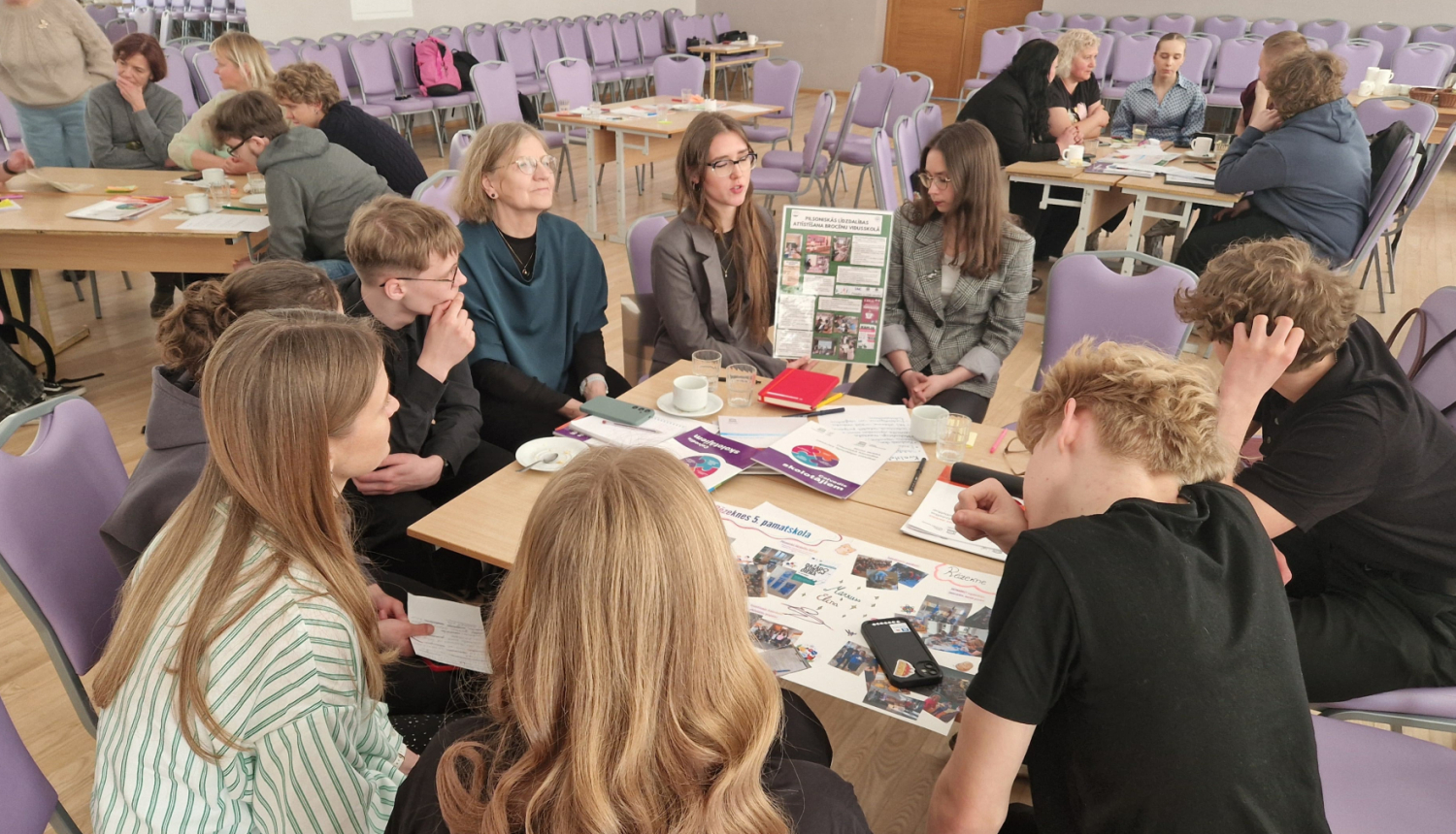 Semināra dalībnieki sēž pie galda apļveida formā un diskutē.